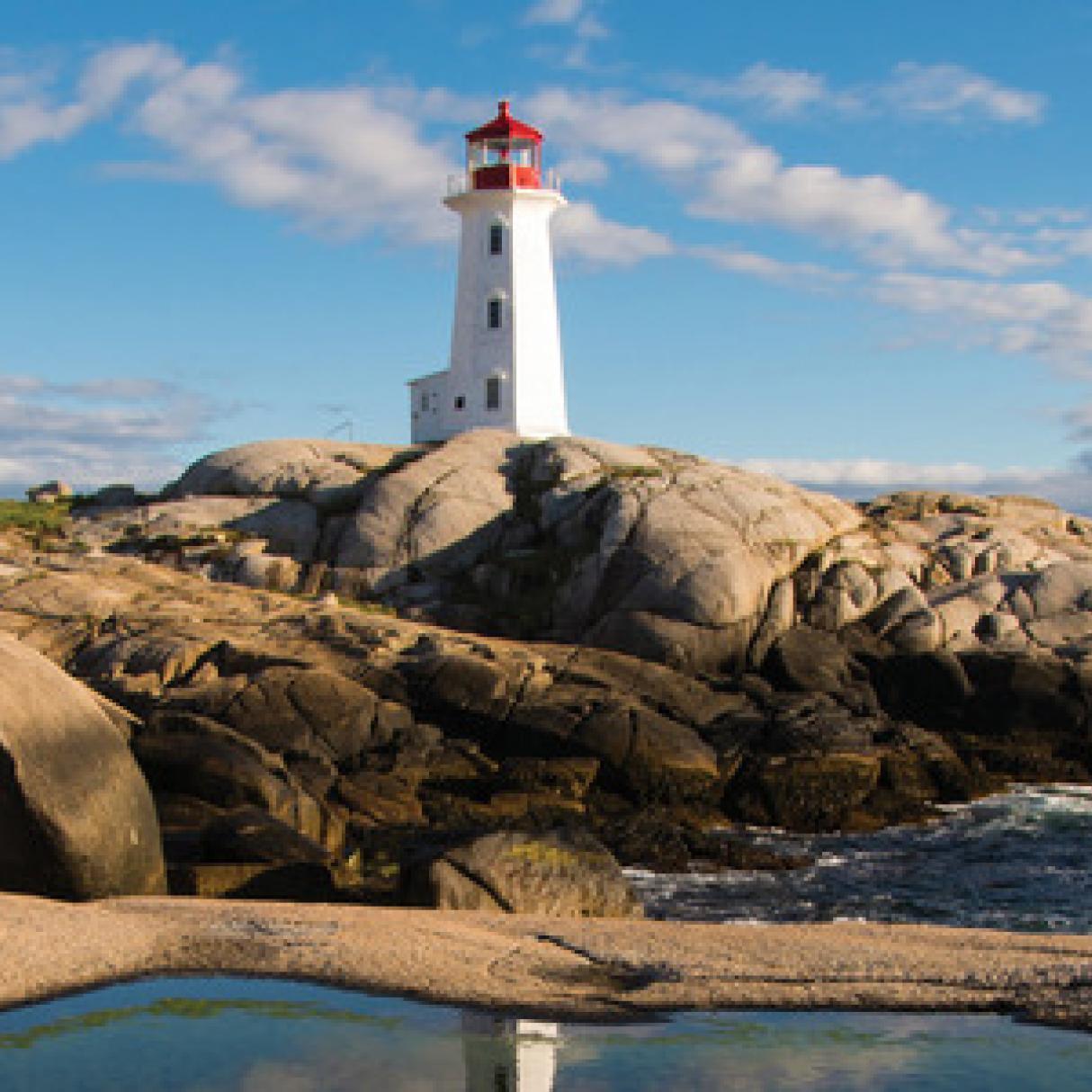 A red and white lighthouse stands upon large brown rocks in the ocean . 